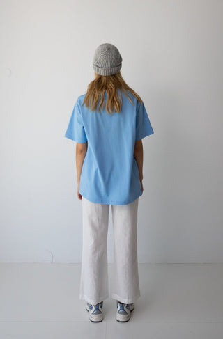 Woman wearing the NorthByOne Lucy Oversized Tee Go North, She Said. Colbalt with white pants and gray beanie standing against a plain background