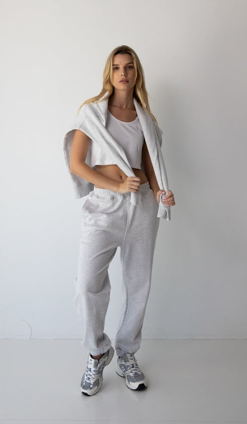 Woman wearing the NorthByOne Emma Baggy Sweat Pant in Marle Grey, with a white crop top and matching sweatshirt draped over shoulders