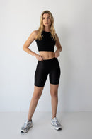 Young woman wearing black NorthByOne Leyla Short Tight and sleeveless crop top standing against plain white background