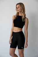 Young woman wearing black NorthByOne Leyla Short Tight and sleeveless black crop top standing against a white wall