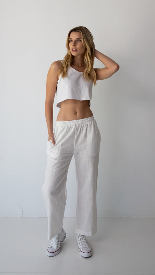 Woman wearing NorthByOne Sadie Linen Pant in white with a white cropped tank top and white sneakers against a plain background
