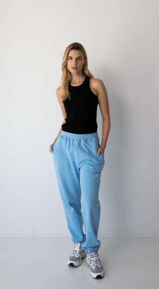 Woman wearing the NorthByOne Emma Baggy Sweat Pant in Colbalt Blue, with a black sleeveless top and sneakers standing against a plain white background