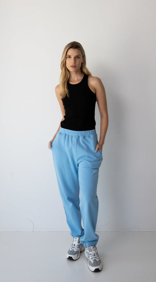 Woman wearing the NorthByOne Emma Baggy Sweat Pant in Colbalt Blue, with a black sleeveless top and sneakers standing against a plain white background