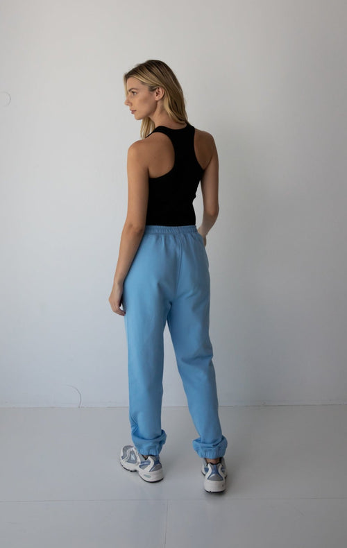Young woman wearing the NorthByOne Emma Baggy Sweat Pant in Colbalt Blue, with a black tank top and sneakers against a plain background