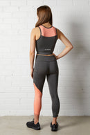 Woman wearing the NorthByOne Cara Three Quarter Tight - Slate Grey / Neon Pink with matching top standing against a white brick wall
