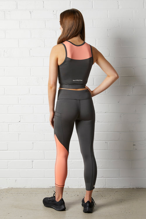 Woman wearing the NorthByOne Cara Three Quarter Tight - Slate Grey / Neon Pink with matching top standing against a white brick wall