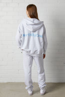 Woman wearing a NorthByOne Olive Zipper Hoodie in Marle Grey with matching pants standing against white brick wall