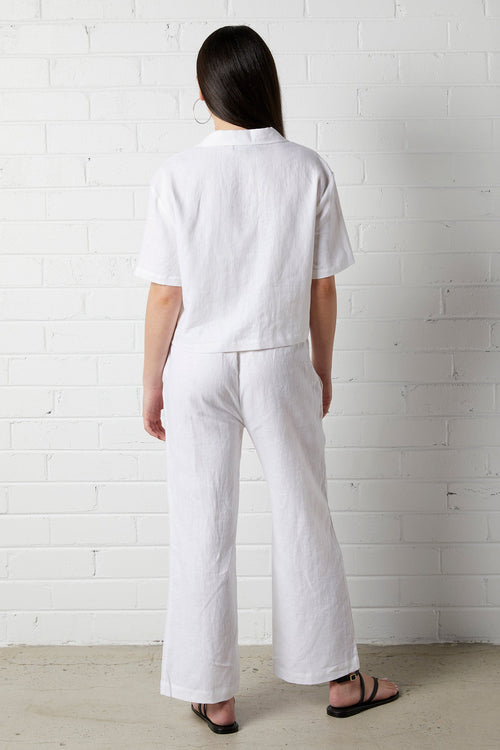 Woman with long dark hair wearing NorthByOne Sadie Linen Pant in white and a matching top standing against a white brick wall
