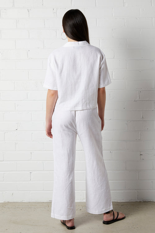 Woman wearing NorthByOneÊ Zoe Linen Shirt in White and matching linen pants standing against a white brick wall