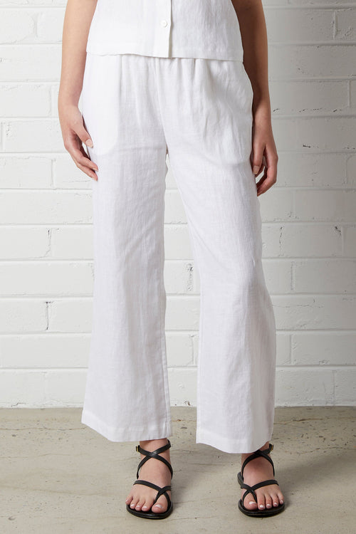 Woman wearing NorthByOne Sadie Linen Pant in white with relaxed fit and elasticated waistband standing against a white brick wall