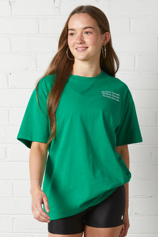 Young woman wearing Lucy Oversized Tee | NorthByOne in Emerald standing against a white brick wall