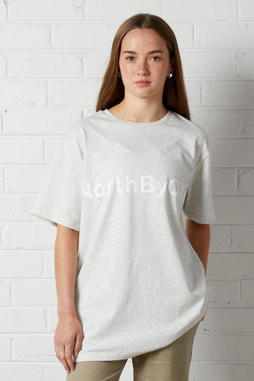 Young woman wearing Lucy Oversized Tee | NorthByOne in Marle Grey standing against a white brick wall