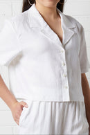 Woman wearing NorthByOne Zoe Linen Shirt in White with short sleeves and button front standing against a white wall