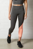 Woman wearing the NorthByOneCara Three Quarter Tight - Slate Grey / Neon Pink with black sneakers standing against a white brick wall