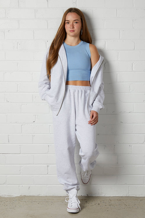 Woman wearing a NorthByOne Olive Zipper Hoodie in Marle Grey over a blue crop top with matching sweatpants standing against a white brick wall