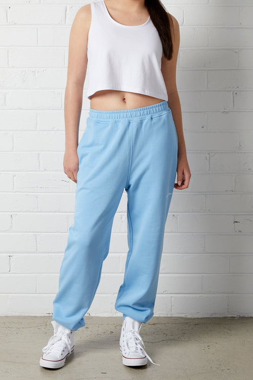 Woman wearing the NorthByOne Emma Baggy Sweat Pant in Colbalt Blue, with elasticated waist and white sneakers standing against a white brick wall