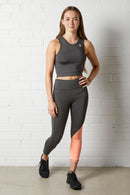 Young woman wearing the NorthByOne Eliza Sports Crop in Slate Grey / Neon Pink and matching leggings standing against a white brick wall