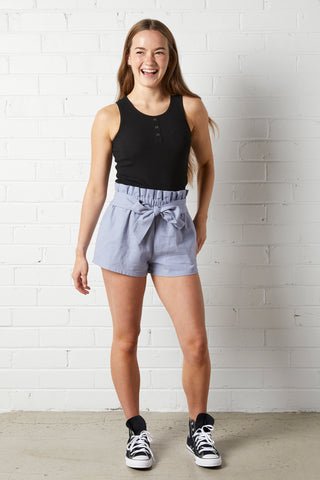 Smiling woman wearing a NorthByOne black tank top and Aria Paperbag Short in an Indigo colour with tie front detail and sneakers
